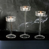 Three clear crystal glass candle holders with lit candles displayed on a dark surface.