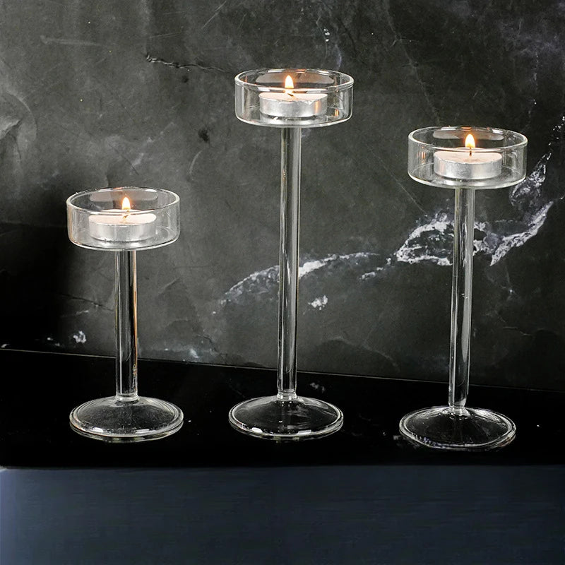 Three clear crystal glass candle holders with lit candles displayed on a dark surface.