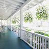 An outdoor porch features white railings and a dark deck with hanging artificial morning glory flowers.