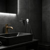 A black vessel sink with a brass faucet is mounted below a dark wall featuring two decorative skull hooks.