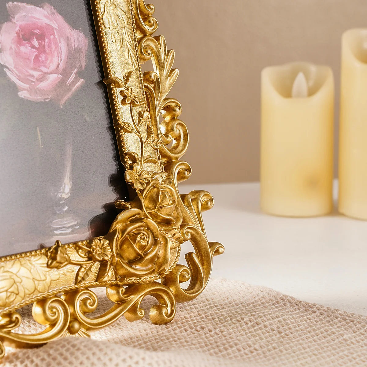 A close-up of a gold-colored, ornate resin photo frame resting on a white surface next to a lit candle.