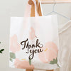 White floral thank you gift bags with pink and green accents hanging on a wooden hanger