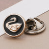 A pair of silver-toned no-sew brooch buttons featuring a black and gold design with a stylized swan motif.