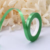 A roll of green satin balloon ribbon unwinding against a background of white flowers.