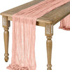 A flowing, semi-sheer gauze table runner in a dusty rose color draped over a wooden table.