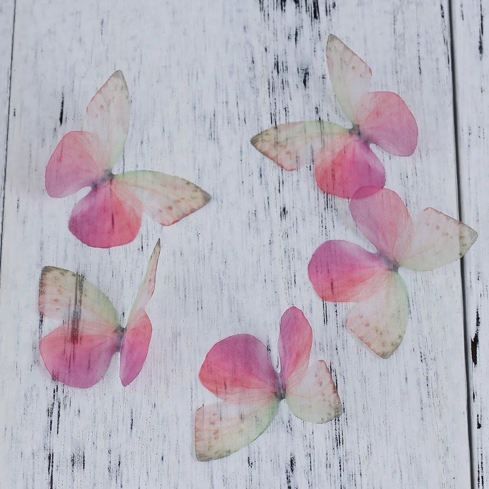 Pink and green organza butterfly embellishments scattered on a white wooden surface.