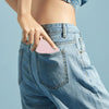 A hand is holding a pink portable folding makeup mirror with an LED light inside the pocket of blue denim jeans.
