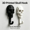 A set of two 3D printed skull hooks, one black and one white, designed as a sturdy wall mount for decor.