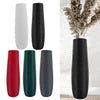 A set of modern tall floor vases in red, dark green, and black, displayed next to a dried floral arrangement.