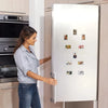 A woman is looking at a refrigerator door decorated with square photo frame magnets.