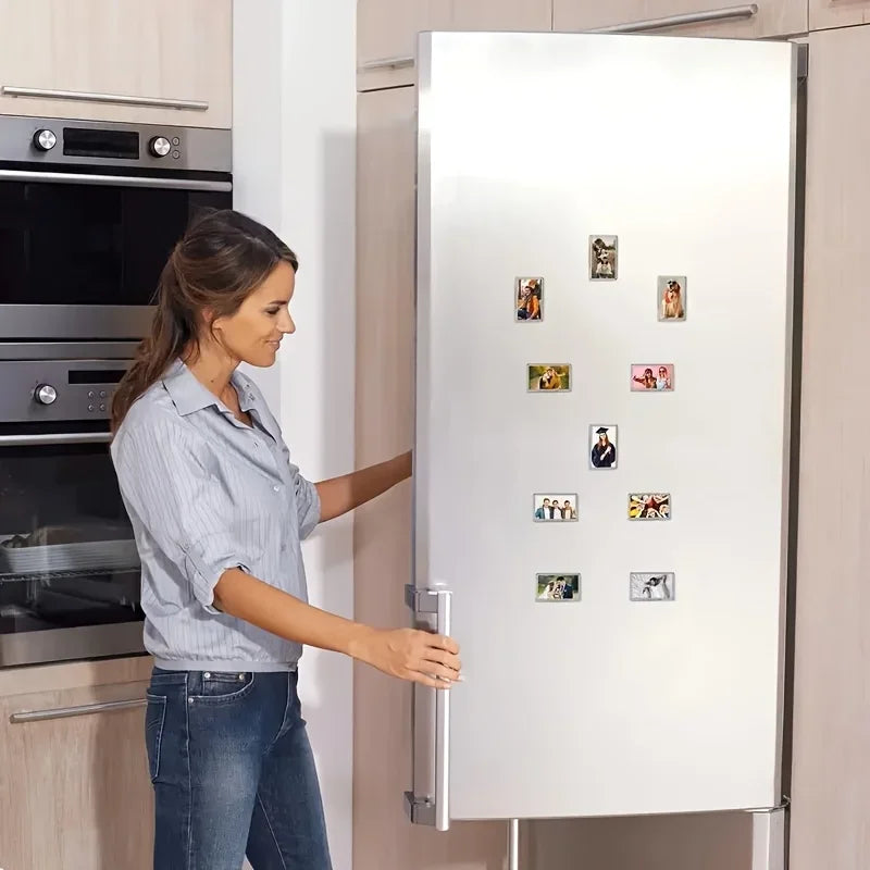 A woman is looking at a refrigerator door decorated with square photo frame magnets.