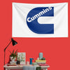 A white flag with a large blue letter C and the word Cummins printed on it, displayed on a red wall.