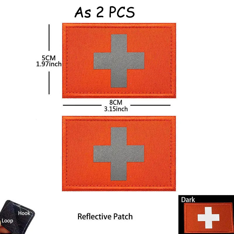 Two orange reflective medical cross patches with a silver cross design and a black loop.