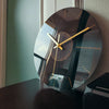 A round, black glass wall clock with gold accents and a white face is displayed on a dark surface.