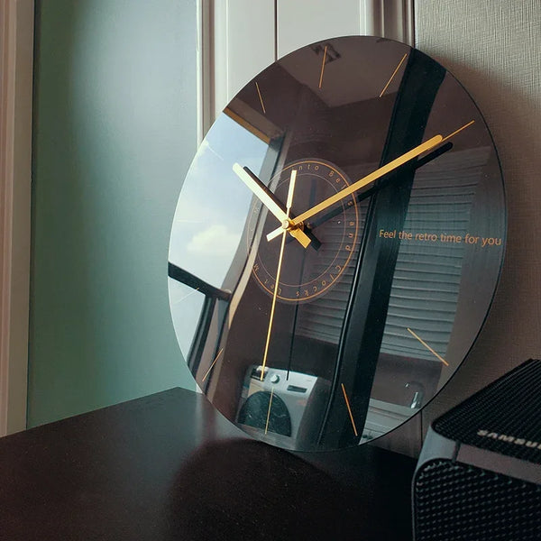 A round, black glass wall clock with gold accents and a white face is displayed on a dark surface.