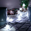 String lights shaped like stars illuminate a plaid fabric next to a dark mug and greenery.