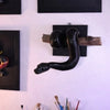 A black ball python wall sculpture is displayed on a white wall among framed art.