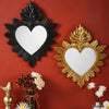 A decorative wall mirror with a heart shape surrounded by ornate flame-like leaves, mounted on a reddish-brown wall.