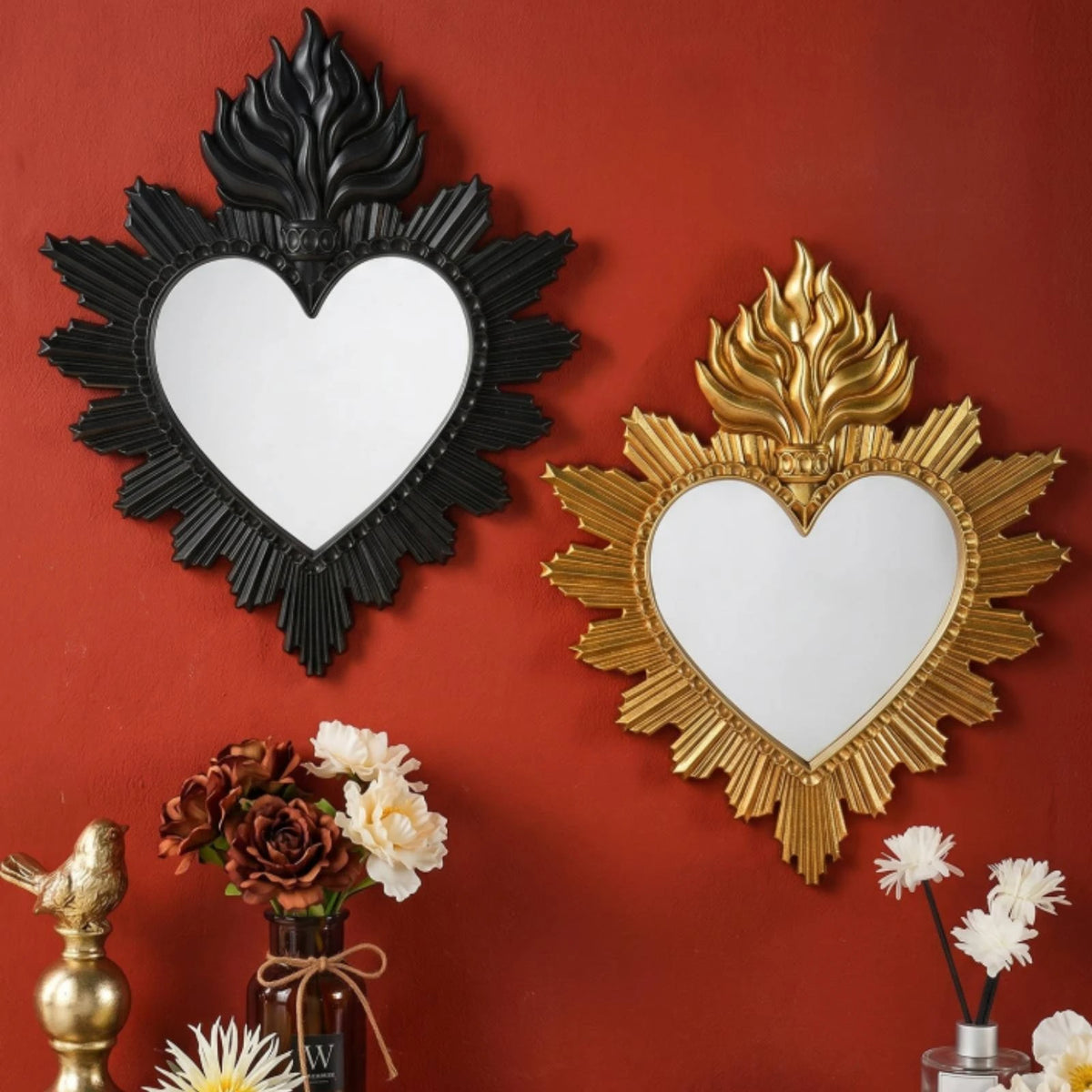 A decorative wall mirror with a heart shape surrounded by ornate flame-like leaves, mounted on a reddish-brown wall.