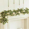 Artificial eucalyptus garland with white roses draped over a white mantelpiece