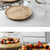 A solid acacia wood cake tray is shown next to a clear glass dome cover on a white marble surface.