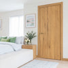 A bedroom scene featuring a bed with white linens and green accents, next to a wooden door and a light rug.