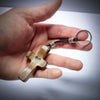 A handcrafted walnut cross keychain with a heart engraving attached to a black cord and silver ring.