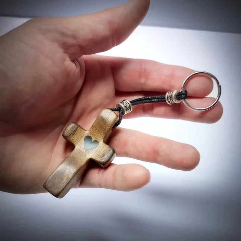 A handcrafted walnut cross keychain with a heart engraving attached to a black cord and silver ring.