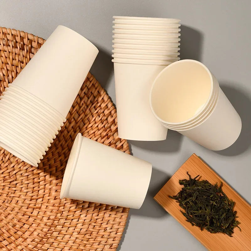 A stack of disposable paper cups in beige and a single cup resting on a woven mat with loose tea leaves.