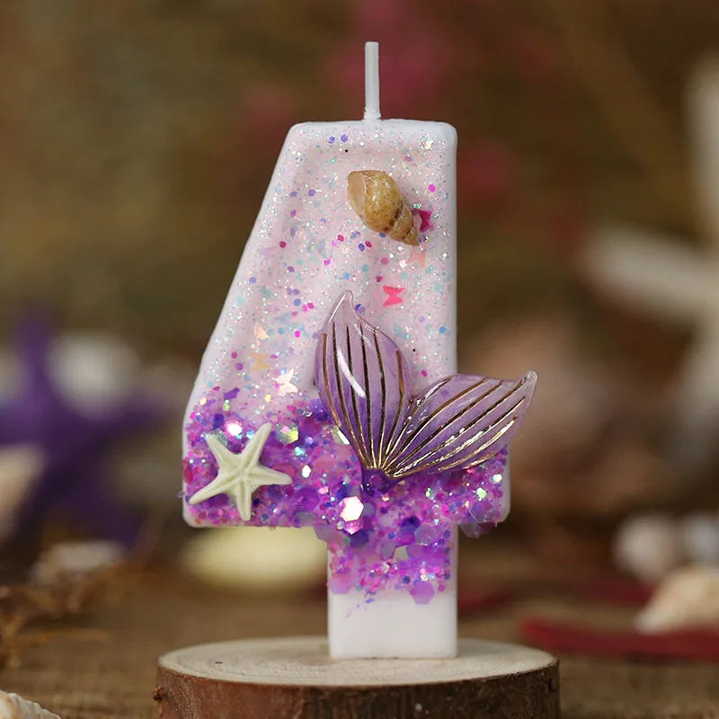 A tall white candle decorated with purple glitter and a gold mermaid tail and starfish design.