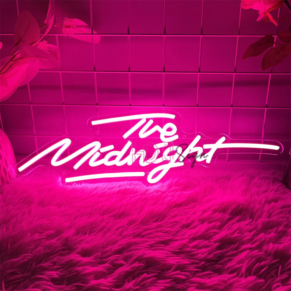 A neon sign spelling out The Midnight glows pink against a textured magenta rug and illuminated by pink tiled walls.