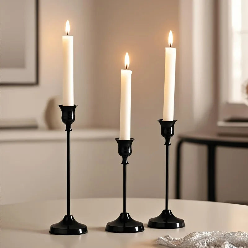 A set of three elegant black metal candlesticks with white candles on a table.