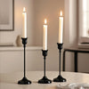 A set of three elegant black metal candlesticks with white candles on a white table.