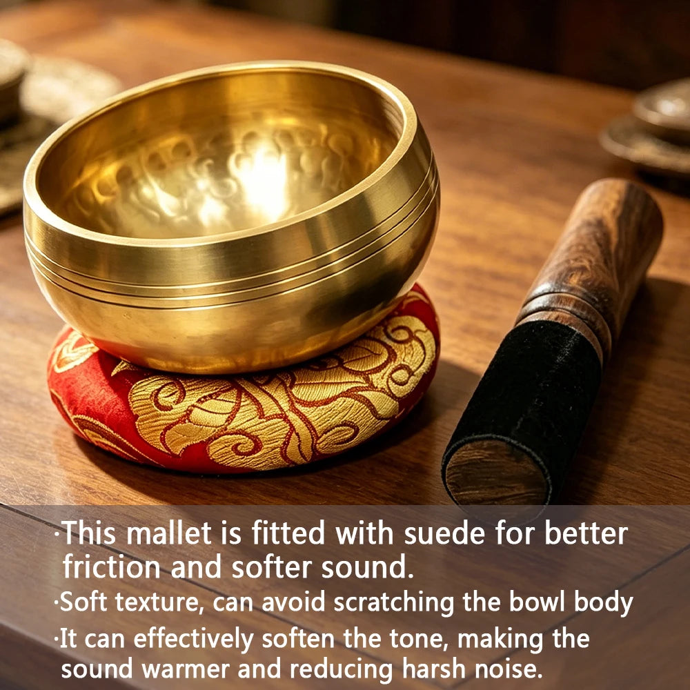 A golden copper singing bowl is shown next to a wooden mallet wrapped in suede on a brown surface.