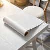 A roll of self-adhesive wood grain wallpaper lying on a white table.