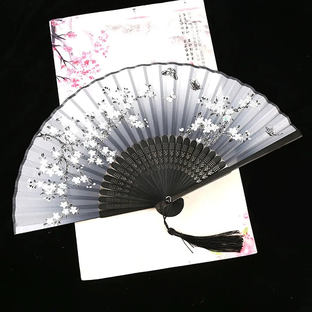 A vintage silk folding fan with gray and white oriental floral patterns is displayed against a light background.