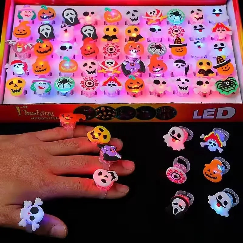 A hand holds various Halloween LED glow rings featuring pumpkin, ghost, and spider designs.
