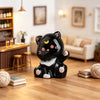 A black and white resin figurine of a sleeping cat with pink accents sitting on a wooden table.