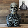 A realistic latex skull mask with intricate bone detailing and a patterned skull helmet displayed on a wooden surface.