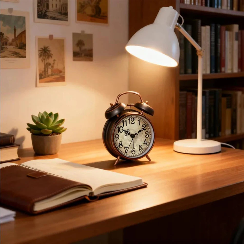 A vintage twin-bell alarm clock with a nightlight sits on a wooden desk next to a stack of books.