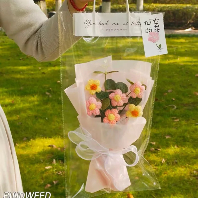 A clear plastic bag containing a handmade crochet flower bouquet of pink and yellow flowers with a handwritten tag.