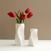 A modern white plastic decorative vase holds a bouquet of deep red tulips against a neutral background.