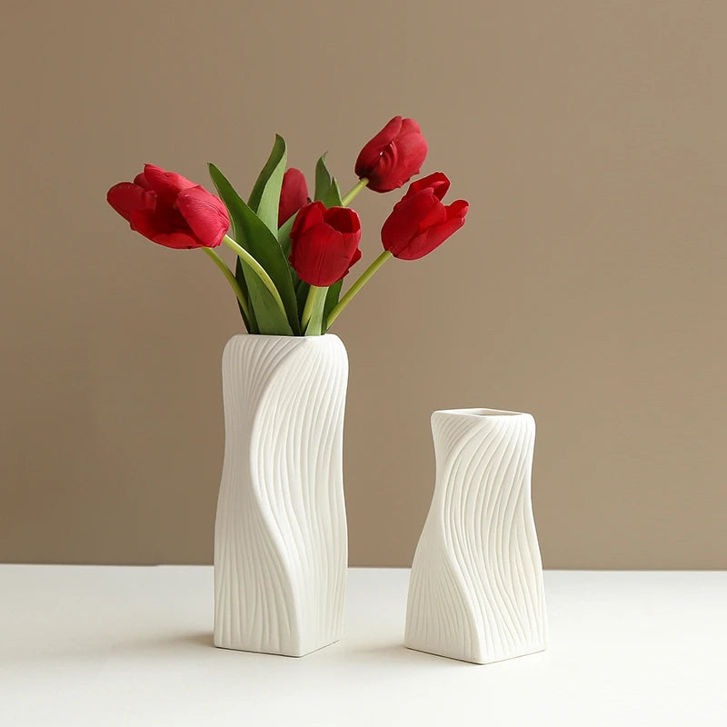 A modern white plastic decorative vase holds a bouquet of deep red tulips against a neutral background.