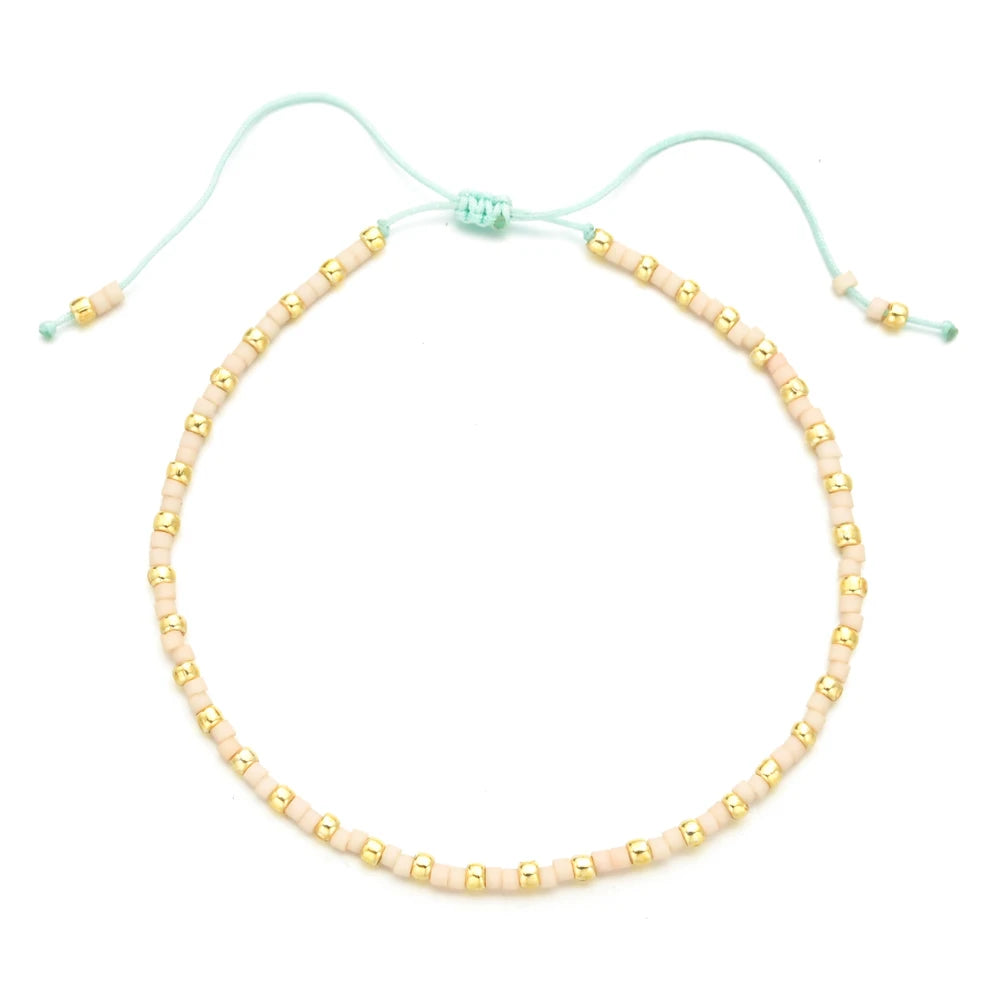 Handmade boho glass bead bracelet with adjustable cord featuring light pink and gold beads.