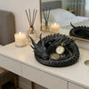 A black dragon design decorative tray for jewelry and small items sits on a white dresser next to a lit candle.