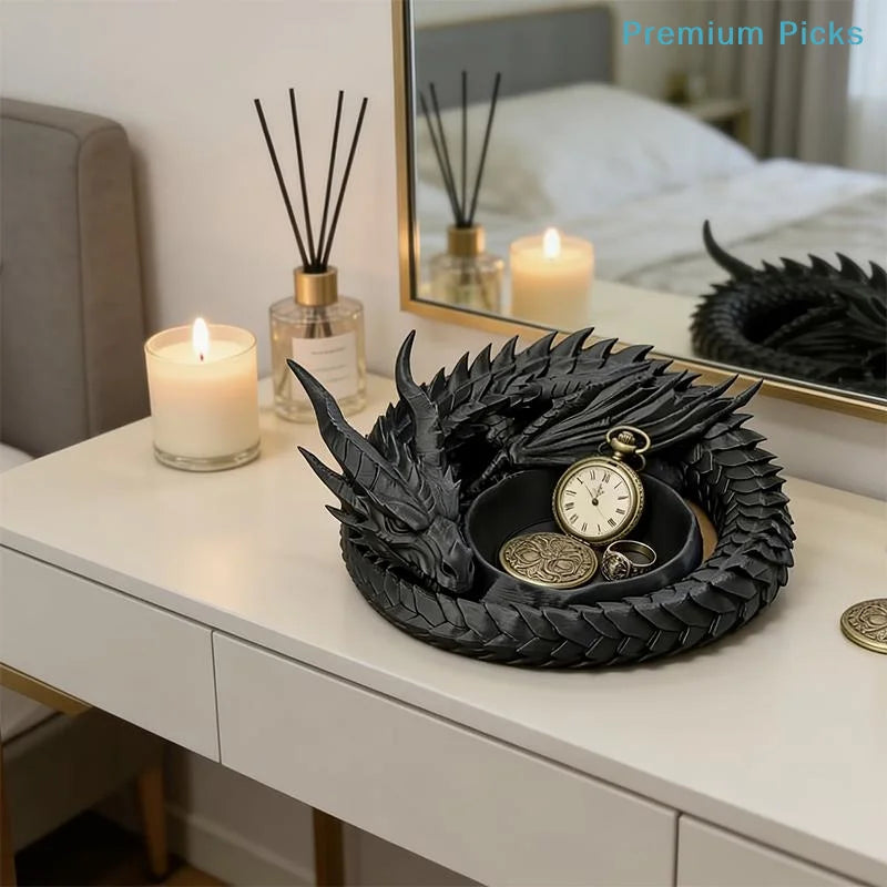 A black dragon design decorative tray for jewelry and small items sits on a white dresser next to a lit candle.