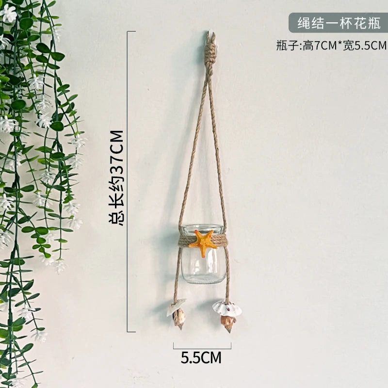A hanging decorative glass terrarium with a starfish and white flowers, suspended by natural twine.