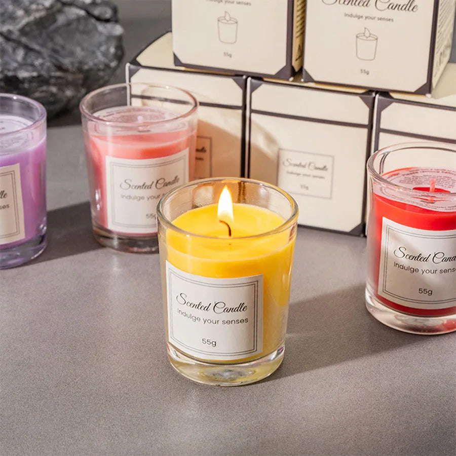 A glass jar of yellow scented candle with a lit wick sits in front of several packaged candles.