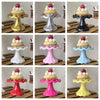 A collection of mini cupcake display stands in various colors and metallic finishes, shown on a wooden surface.