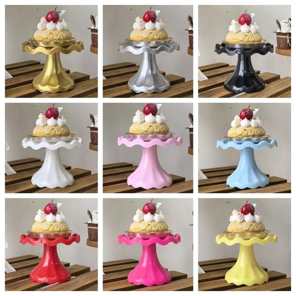 A collection of mini cupcake display stands in various colors and metallic finishes, shown on a wooden surface.